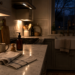 Quiet kitchen at night with soft under-cabinet lighting, a linen towel, dish brush, amber soap bottle, and the evening sky visible through the window.
